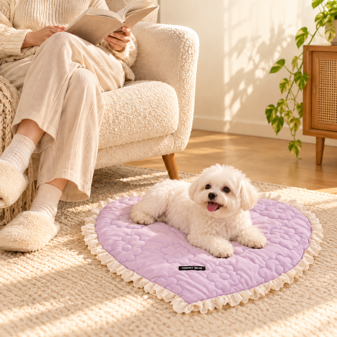 White dog resting on the Purple heart-shaped mat with large floral quilting and its original black fabric label beside a seated owner