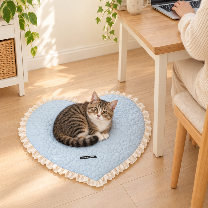 Cat resting on the Blue heart-shaped floral-quilted mat beside a home desk, with the original black fabric label visible