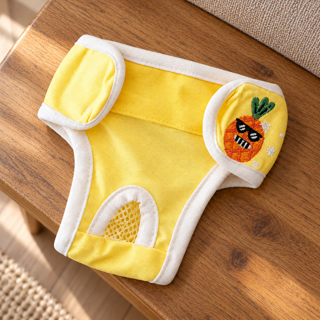 Yellow dog diaper pants with original pineapple embroidery, mesh tail opening and white waist tabs on a home bench.