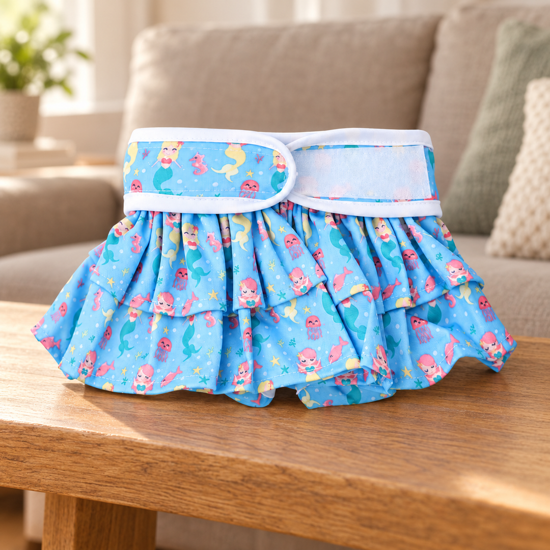 Fish-print pet diaper pants with ruffled trim on a warm wood surface.