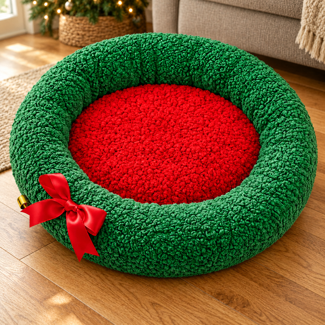 Green Christmas wreath pet bed with red center, red bow and gold bell in a warm home interior.