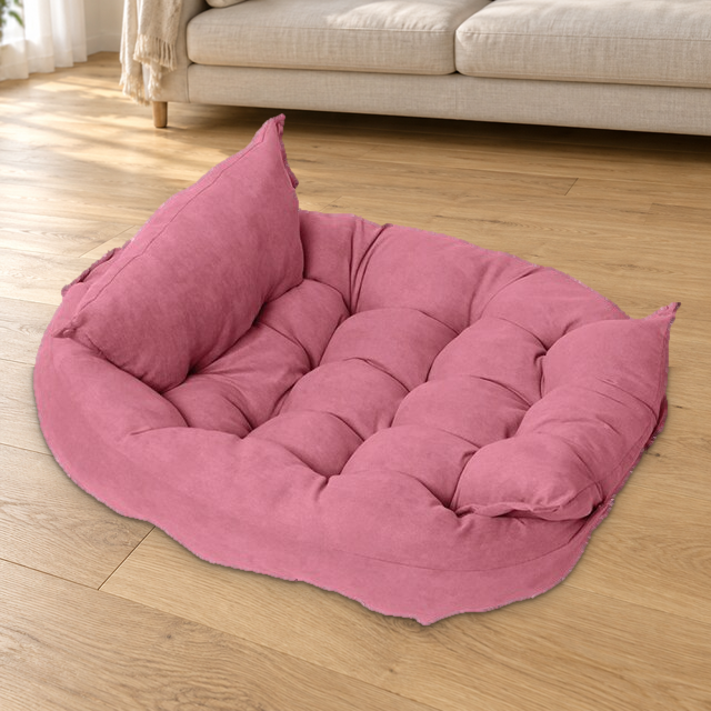Pink foldable quilted pet bed with raised padded sides resting on a wood floor beside a cream sofa