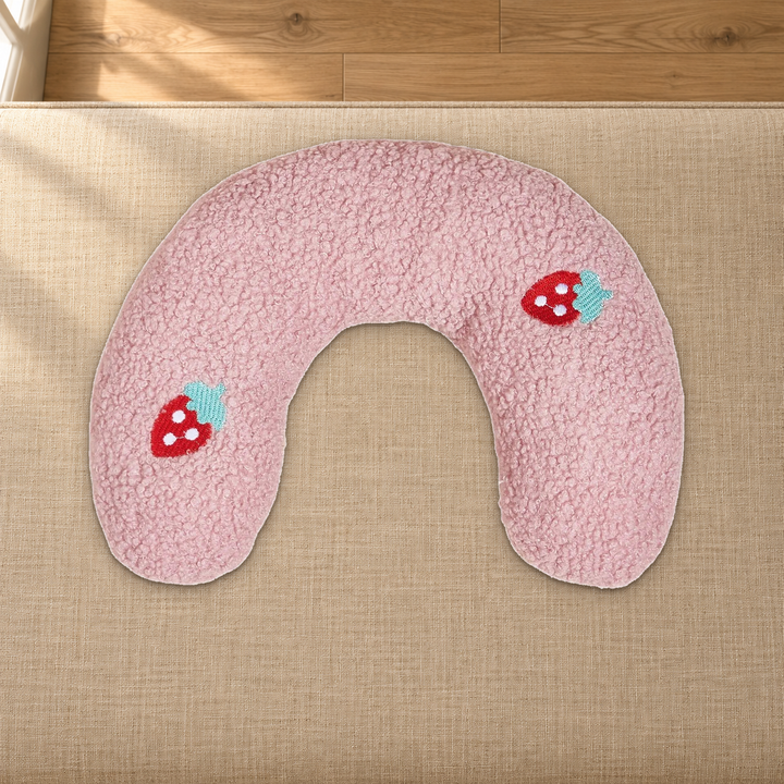 Pink U-shaped pet pillow with strawberry embroidery resting on a fabric-covered bench