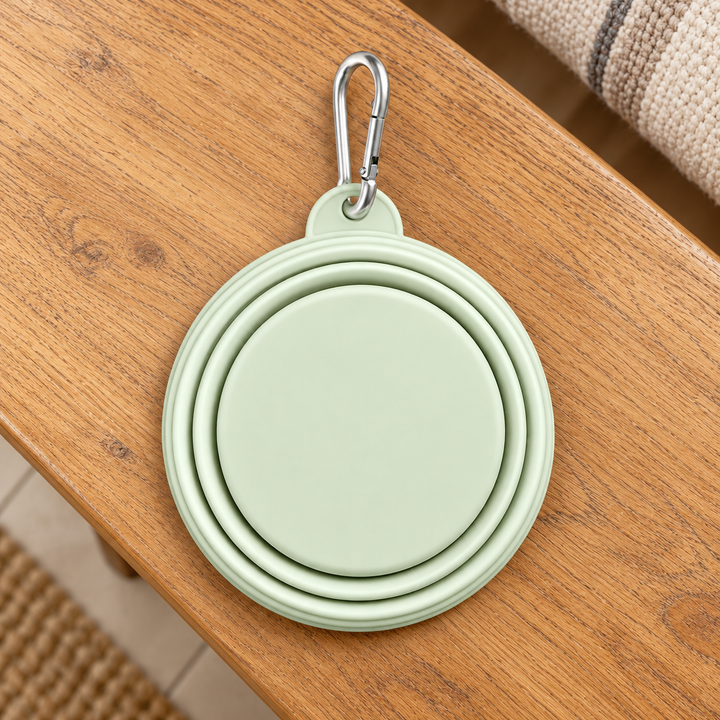 green folded silicone travel bowl with silver carabiner on a warm wooden home bench.