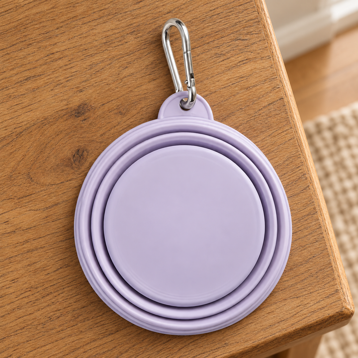 Purple 350 ml silicone travel bowl folded flat with its silver attachment clip on an oak home console.