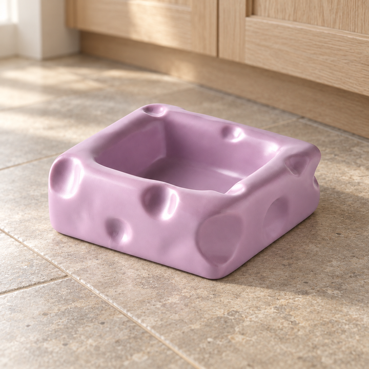 Purple large square cheese-shaped ceramic pet bowl on a natural stone kitchen floor.