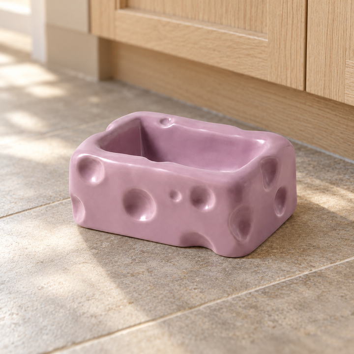 Purple rectangular cheese-shaped ceramic pet bowl on a natural stone kitchen floor.