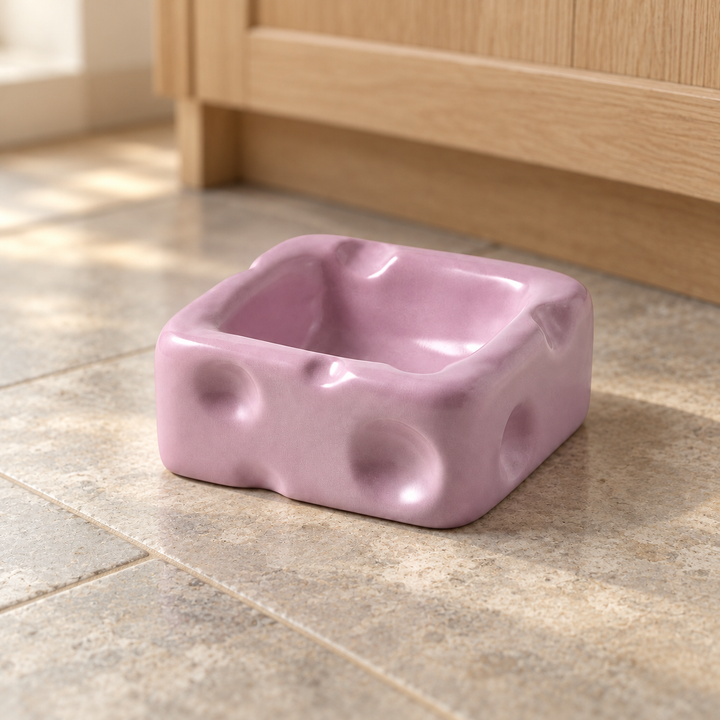 Purple small square cheese-shaped ceramic pet bowl on a natural stone kitchen floor.