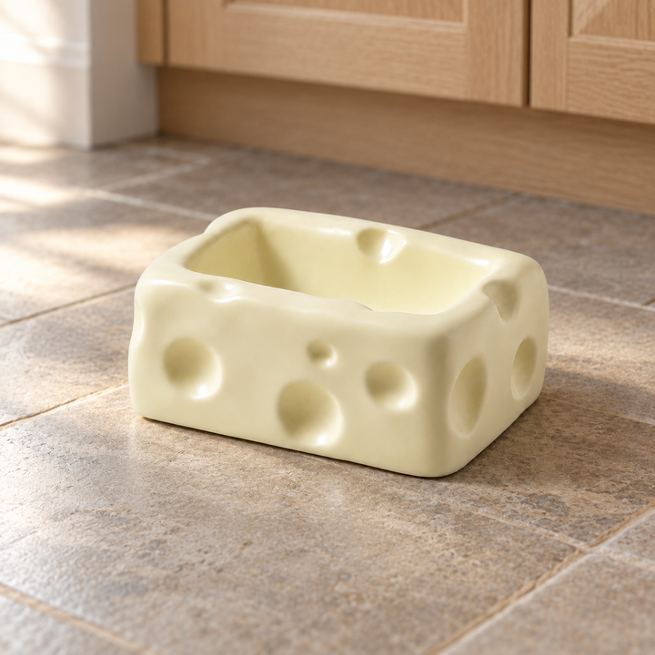 White rectangular cheese-shaped ceramic pet bowl on a natural stone kitchen floor.