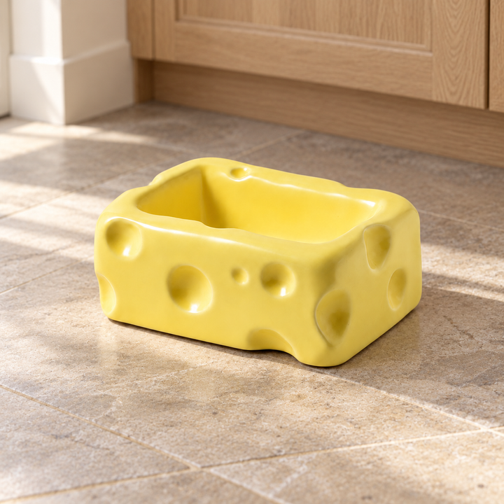 Yellow rectangular cheese-shaped ceramic pet bowl on a natural stone kitchen floor.