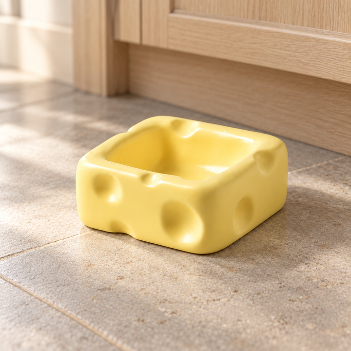 Yellow small square cheese-shaped ceramic pet bowl on a natural stone kitchen floor.