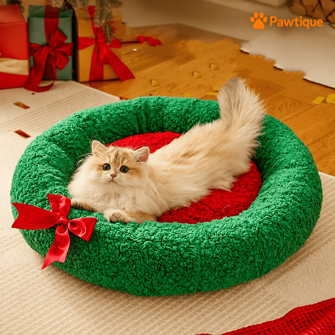 Cat resting in the open red center of the green wreath-design bed.