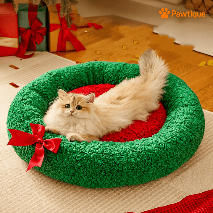 Cat resting in the open red center of the green wreath-design bed.