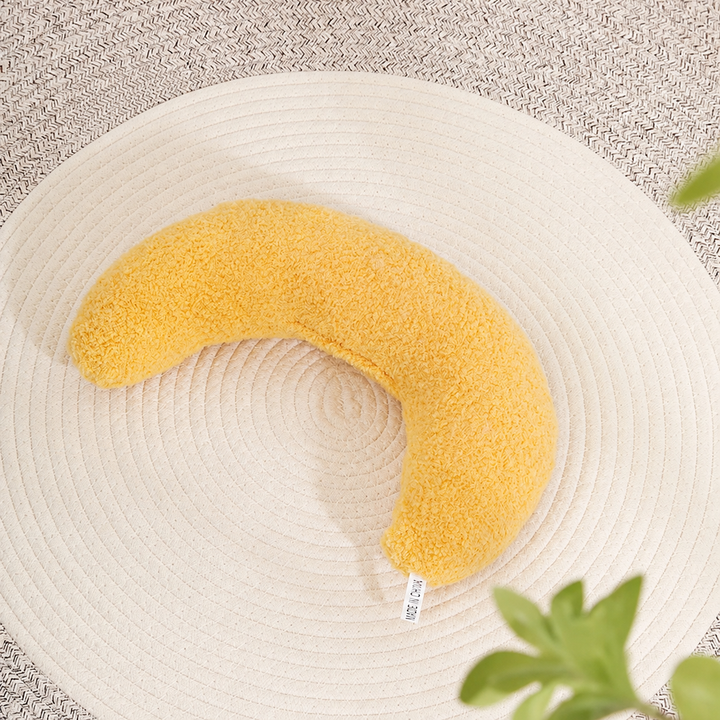 Yellow plain crescent pet pillow on a woven mat