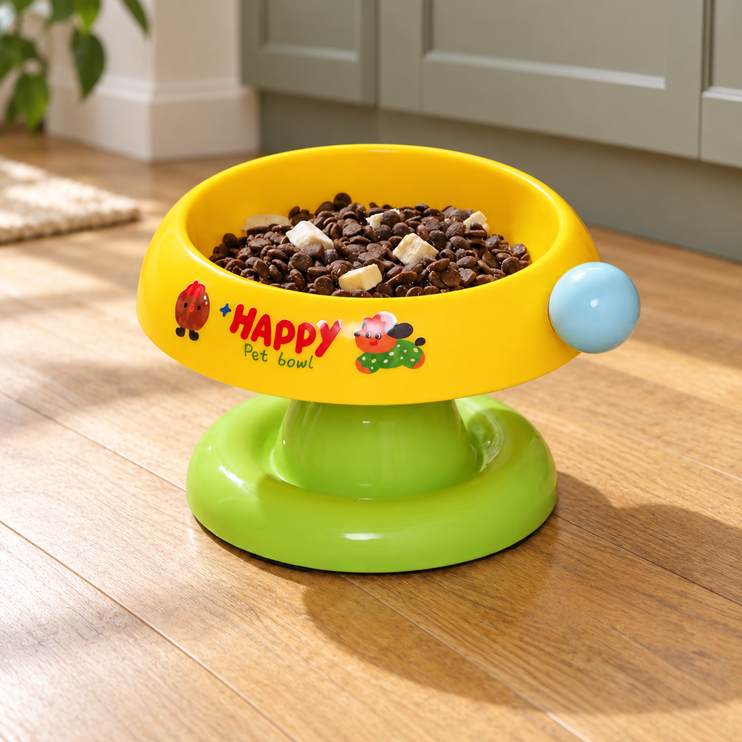 Yellow tilted pet bowl with a green pedestal, light blue side ball and original illustrated print, shown in a home feeding corner.