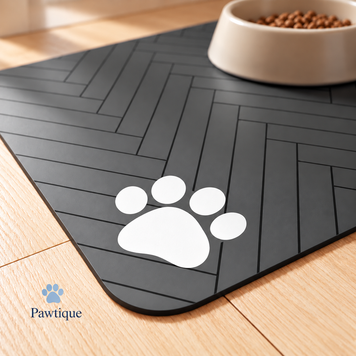 Close-up of the feeding mat rounded corner, black herringbone lines and white four-toe paw motif, with a bowl in the background.