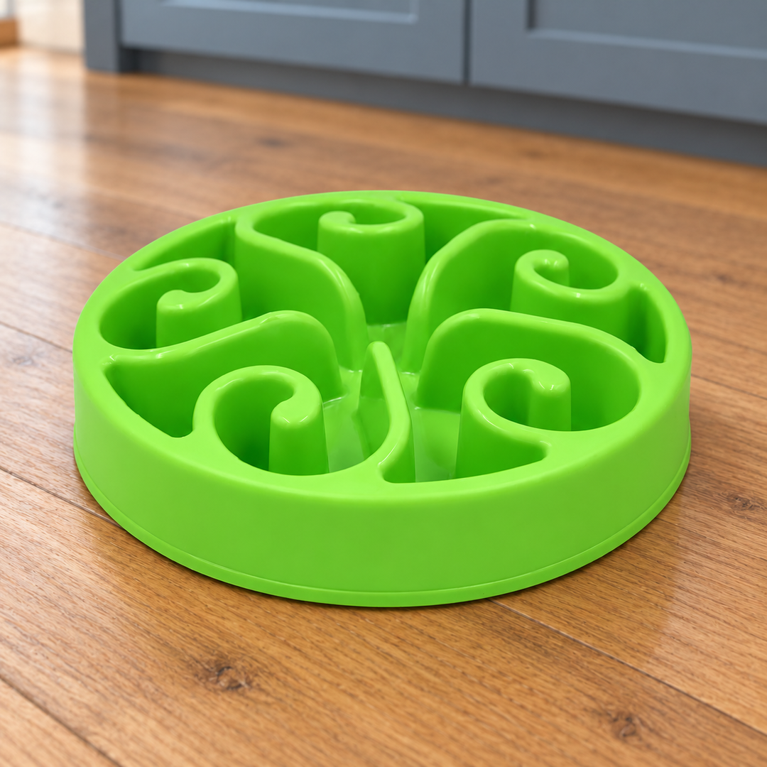 Green slow-feeder dog bowl with five curled spiral walls on a natural wood kitchen floor.