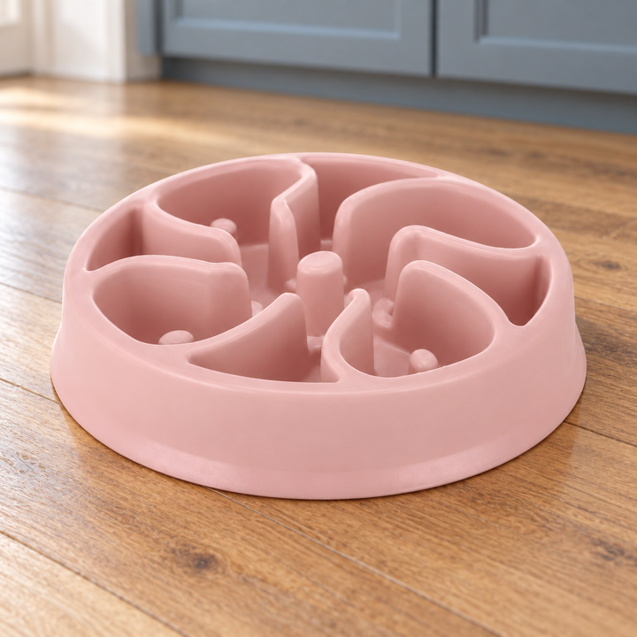 Pink slow-feeder dog bowl with broad curved divider walls and distinct raised posts on a natural wood kitchen floor.