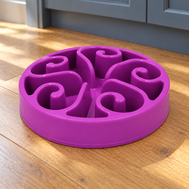 Purple slow-feeder dog bowl with five curled spiral walls on a natural wood kitchen floor.